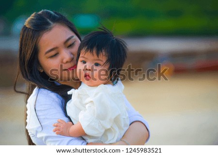 young happy Asian Chinese woman mother of adorable baby girl holding her sweet little daughter in her arms taking a walk at tropical beach enjoying summer holidays trip together