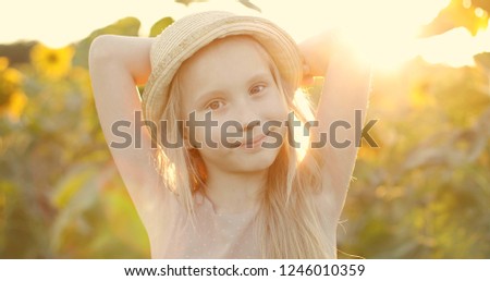 Happy blonde girl sunbathing in a field with yellow sunflowers. Light flare, lens glare. 
