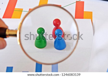 A young man is holding a magnifying glass in his hand, looking at statistic figures - a business concept on the subject of sampling and selecting the right target group and examining it Royalty-Free Stock Photo #1246083139