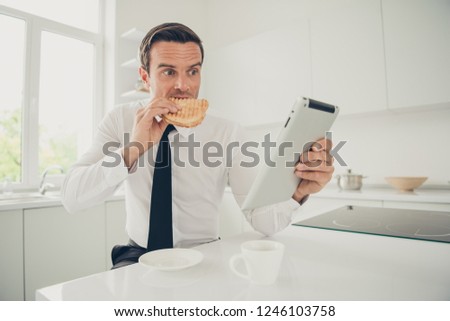 Portrait of nice lovely attractive handsome focused concentrated serious man business shark eating baked roasted sandwich reading e-book at light modern interior kitchen
