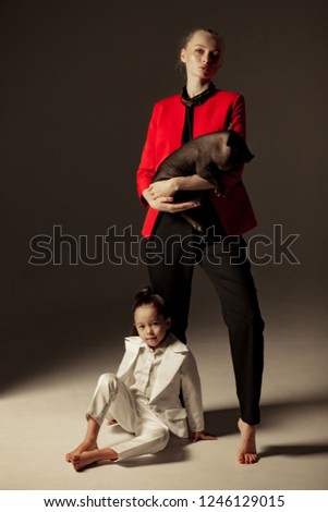 Young mother with black vietnamese piglet on her hands is posing in studio with her little daughter. Concept of the Chinese New Year of the Pig.