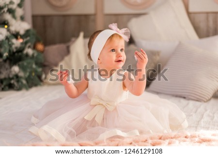 Little baby girl is playing near the Christmas tree, cozy winter season, tenderness.