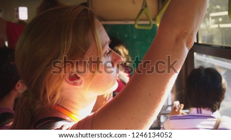 A tired woman rides on a bus while standing and holding onto a rail