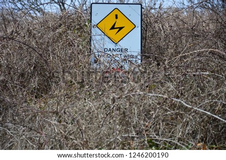 yellow sign warning of electricity in dry bushes