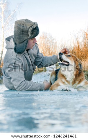 young man on a walk with a dog-lying on the ice and stroking the dog on the head