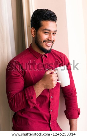 Attractive Arabian and Arabic Egyptian hansom man model holding on his hand a cup of tasty and hot delicious coffee and relaxing in the hotel  room in Alexandria in Egypt at middle east, Africa