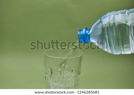 clear water flows from a plastic bottle into a glass on green background
