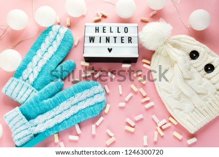 Warm, cozy winter clothing hat, mittens, lightbox and christmas decorations  as frame on pastel pink background. Christmas concept flat lay. Hello winter title