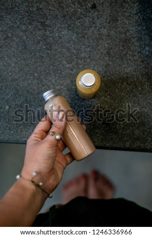 Woman's hand holding spa cosmetics in plastic bottle against dark gray backgroud, bathroom interior. Beauty blogger, salon therapy, branding mockup, package, minimalism concept. Top view