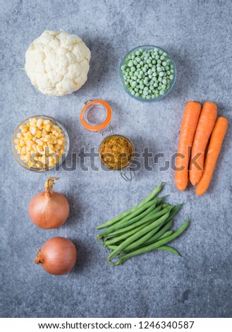 Ingredients for onion curry paste on light grey background. Picture of two onions, cauliflower, peas, corn, green beans and carrots on grey background.