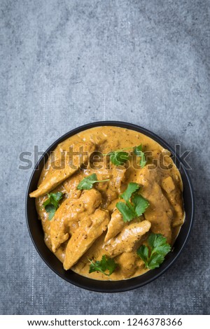 Chicken korma curry at center in a black bowl and light grey background. Round bowl of Indian chicken korma curry with fresh coriander leaves. Royalty-Free Stock Photo #1246378366