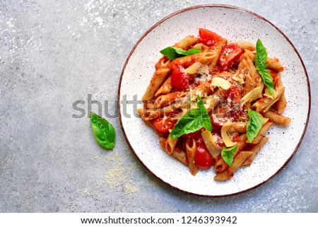 Penne pasta with tomato in red sauce on a white plate over light grey slate, stone or concrete background.Top view with copy space. Royalty-Free Stock Photo #1246393942