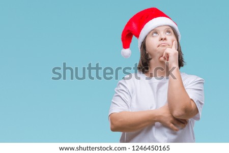 Young adult woman with down syndrome wearing christmas hat over isolated background with hand on chin thinking about question, pensive expression. Smiling with thoughtful face. Doubt concept.