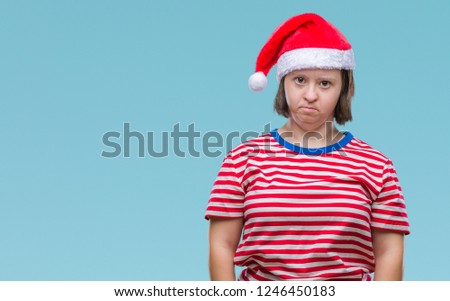Young adult woman with down syndrome wearing christmas hat over isolated background with serious expression on face. Simple and natural looking at the camera.