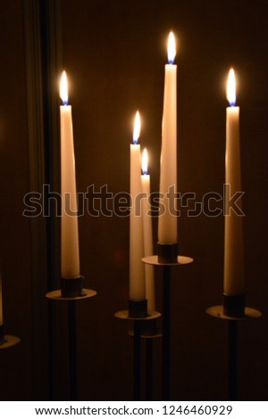 A lot of candles in dark room, five or six white and tall standing candles with flame