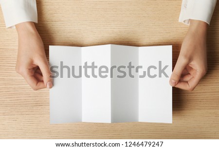 Woman holding blank brochure mock up on wooden table, top view