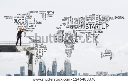 Businessman in helmet writing business-related terms in form of world map while standing on broken bridge with cityscape on background. 3D rendering.