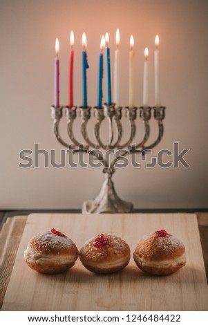 Image of jewish holiday Hanukkah background with menorah traditional candelabra also called a Hanukiyah, jelly or jam doughnut sufganiyot and burning candles.Retro style. Toned image.