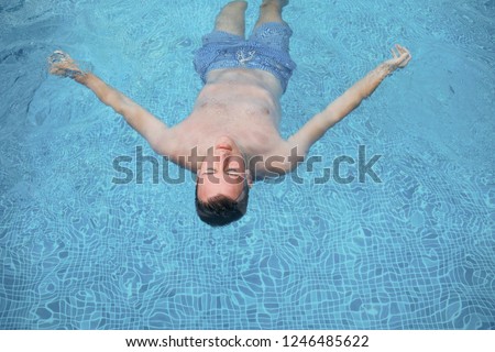 beautiful bright modern photo of young Caucasian handsome man in blue swimsuit shorts in blue pool floating on his back,relaxing and enjoining sunny summer hot day in spa 