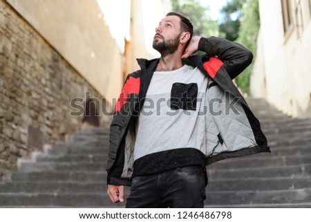 Man in black jeans and green jacket posing in front of old europe buildings. Fashion stills of male model in jacket.