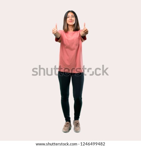 Full body of Young girl with pink shirt giving a thumbs up gesture with both hands and smiling. Cheerful expression