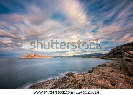 Slow exposure image of evening sun lighting up wispy clouds on the red rock of La Pietra in Ile Rousse in the Balagne region of Corsica