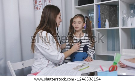 Woman doctor listening to little girl with phonendoscope in the office in a medical clinic