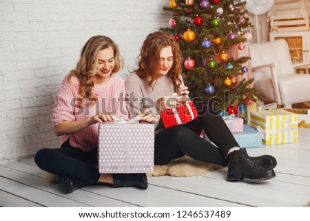 two beautiful and stylish girls sitting by the Christmas tree with gifts
