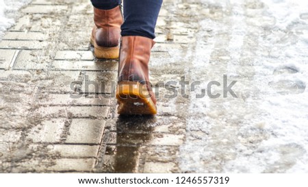 Walk on wet melted ice pavement. Back view on the feet of a man walking along the icy pavement. Pair of shoe on icy road in winter. Abstract empty blank winter weather background