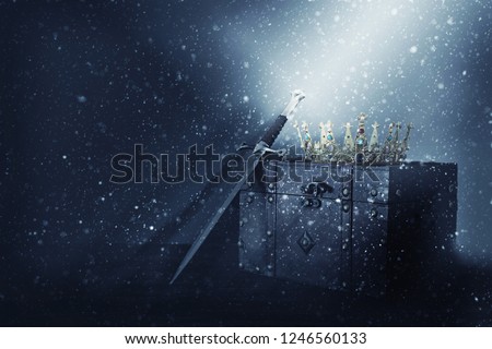 mysterious and magical image of old crown, wooden chest and sword over gothic black background. Medieval period concept