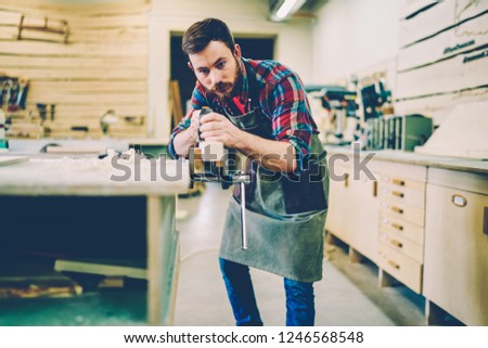 Serious male master concentrated on repairing and doing furniture with equipment in working place, professional man joiner owning carpentry manufacture business making restoration job with timber