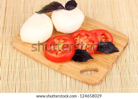 tasty mozzarella with tomatoes on chopping board on mat
