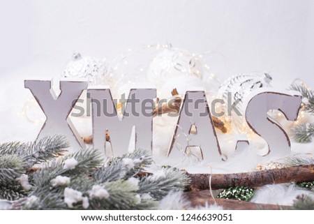 Wooden word Xmas,   branches fur tree and balls on  white  background against  white wall. Selective focus. Winter holidays, Christmas concept. 