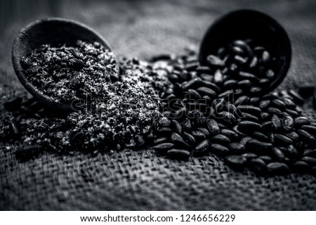 Close up of brown colored dried custard apples or sitaphal or sugar apple seeds in a black colored clay bowl and its powder of grounded seeds in a brown colored clay bowl.