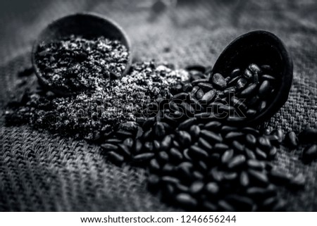 Close up of brown colored dried custard apples or sitaphal or sugar apple seeds in a black colored clay bowl and its powder of grounded seeds in a brown colored clay bowl.