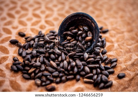 Close up of brown colored dried custard apples or sitaphal or sugar apple seeds in a black colored clay bowl on a brown colored surface.
