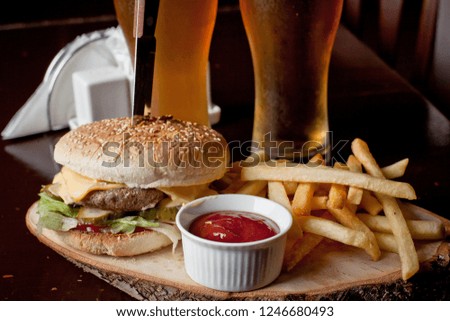 hamburger with juicy meat lies on a table against the background of glasses of beer and pieces of zhereny potatoes