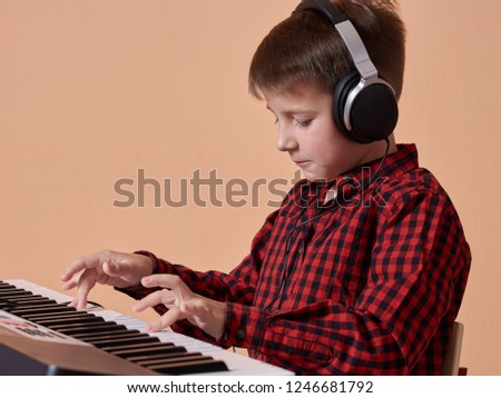 Caucasian boy is practicing to play electric piano. He is listening to headphones and playing instrument. Portrait against peach background.