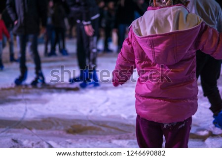 Image of people skating on ice at Christmas time. Little girl with shoulders in the foreground