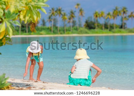 Little cute girls drawing picture on the sand on white tropical beavh beach