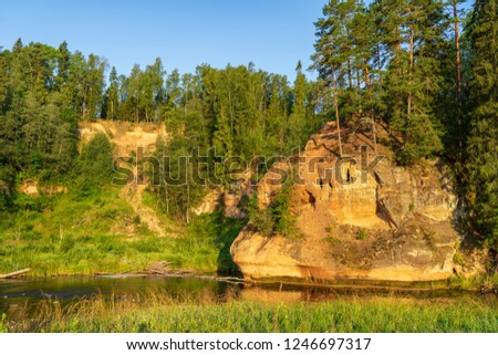 water stream in river of Amata in Latvia with sandstone cliffs, green foliage in summer morning