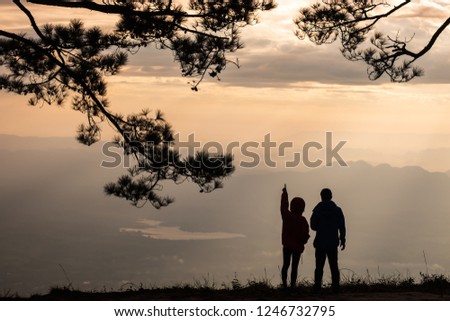 silhouette of lover couple at the cliff viewpoint in the morning sunrise framing with pine.
