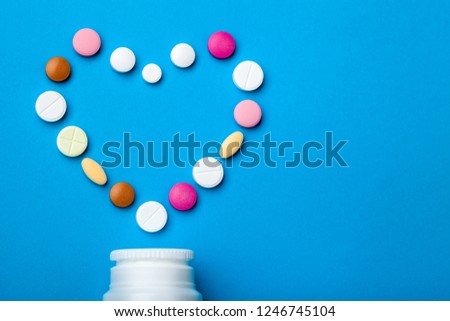 Close up concept for a cardiological theme plastic white bottle with colored pills in the form of a heart on a blue background with free  copy space for text.