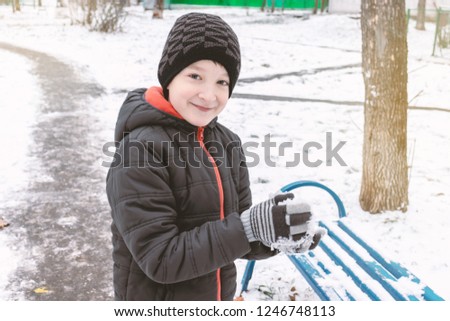 Caucasian boy sculpts snowballs, outdoor winter activities, sports concept.