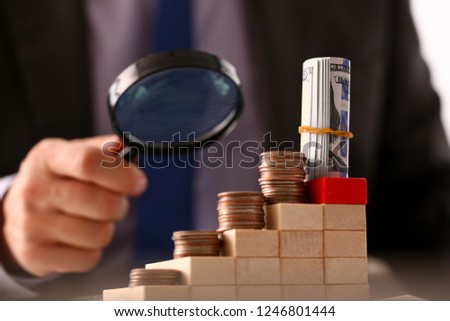 Hand businessman in suit hold lens background looking through money towers closeup search business concept Royalty-Free Stock Photo #1246801444