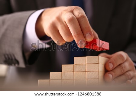 Male hand holds red wood block of stair finish next step rare progress personnel talent authority hot pyramid background on ladder different insurance concept closeup Royalty-Free Stock Photo #1246801588