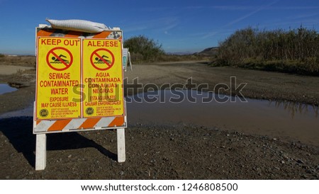 Yellow signs next to dirty puddle warn of dangerous sewage contamination on hiking trail near Tijuana River