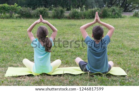 boy and girl do yoga sitting on a green lawn