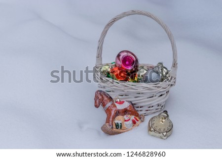 The basket is filled with old glass Christmas tree decorations on white snow on a winter evening. 