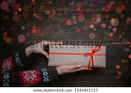 Close up shot of female hands holding small gifts box wrapped with red ribbon. Small gift in the hands of a woman indoor. Shallow depth of field with focus on the little box. Toned image.